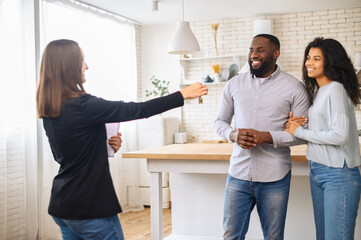 Relocation concept. A smiling cheerful multiracial couple receives the keys to a new home from a real estate agent, smiling African man and woman rent new apartment