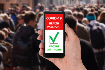 Person using digital health vaccine immunity passport app in mobile phone for restaurant visits, shopping or travel during covid-19 pandemic. Crowd of people on shopping street blurred in background.