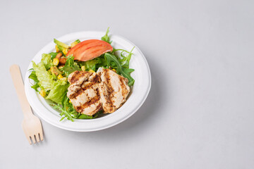 Meat diet salad with grilled chicken, tomatoes, arugula on light background. Healthy lunch. Take away food in eco paper plate. Concept eco restaurant delivery, environment protection, plastic free