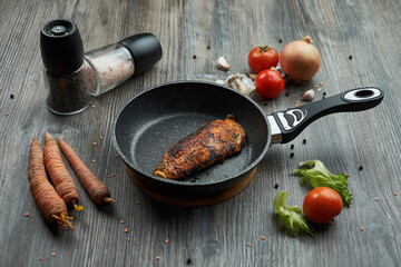 fried chicken breast in a black pan on the table. around vegetables and spices