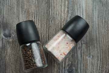salt shaker with pink salt and pepper shaker lie on a gray wooden table. view from above