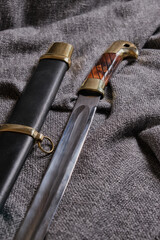 Fragment of a Cossack saber with a scabbard on a rough, dark fabric background. Cold, traditional weapons.