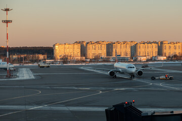 An airliner standing alone near the airport in the early winter morning. In the background, residential areas. Shooting through the airport terminal window. Daybreak in the almost empty airport.
