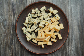 brown plate on which two types of cheese cut into cubes top view