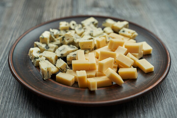 brown plate on which two types of cheese cut into cubes. one with blue mold the second yellow.