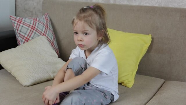 a little girl sits on the sofa among the pillows