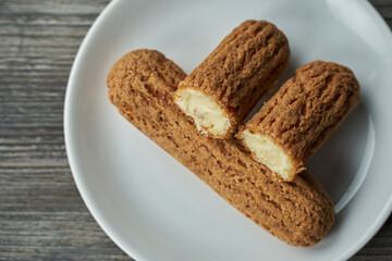 two eclairs with custard inside on a white plate. one is cut in half and lies on the second. the plate stands on a gray wooden table. view from above