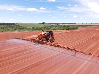 Imagem aérea de trator em ambiente agrícola durante pulverização da lavoura.