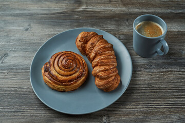 puff pastry. two buns of different shapes on a plate. one round the other elongated and a mug with coffee
