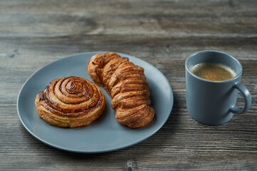 two puff pastry buns on a plate and next to a mug of coffee