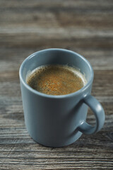 aromatic black coffee with froth in a gray mug on a wooden gray table