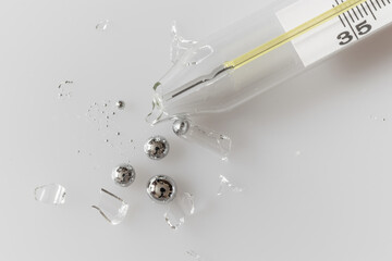 Broken glass mercury thermometer on light grey surface. Mercury drops with glass fragments. Mercury...