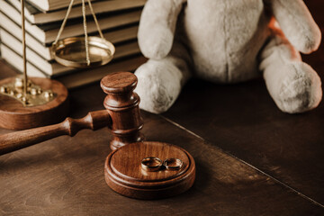 Divorce concept. Wooden gavel, rings and teddy bear as symbol of child on a desk