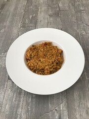 A bowl of chicken tikka biryani against a wooden background 