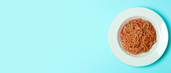 Spaghetti pasta with tomato sauce on a white plate on a blue empty background. Italian pasta dish background. Italian cuisine and food