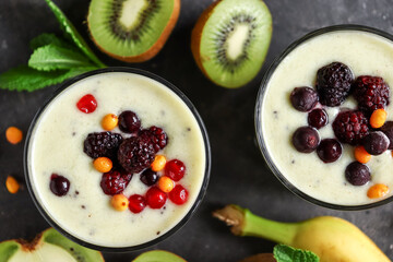 Yogurt with berry and kiwi in a glass. Fruit and berry smoothie. Milkshake with kiwi, raspberry, blueberry and banana. Top view Healthy food. Dark background. Copy space.