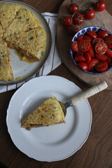 Spanish Omelette dinner from top view. Sliced tortilla on table with a served slice. Side salad made of tomatoes. 