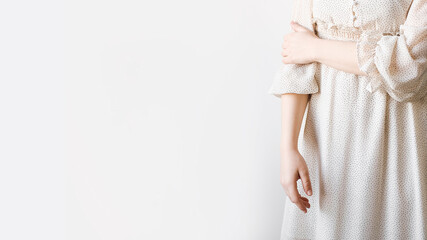 A woman in a light summer silk dress poses against a light wall.