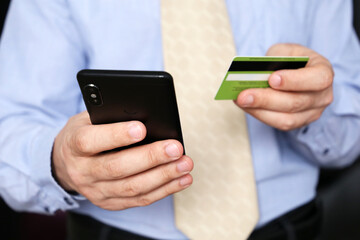 Man in office clothes holding credit bank card and smartphone in hands. Concept of online shopping and payment, financial transaction