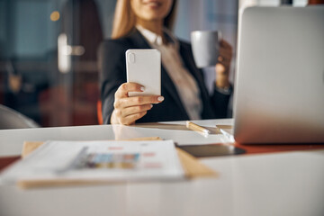 Joyous office worker using her smartphone during the coffee break