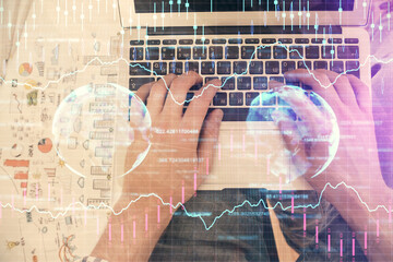 Double exposure of man's hands typing over laptop keyboard and forex chart hologram drawing. Top view. Financial markets concept.