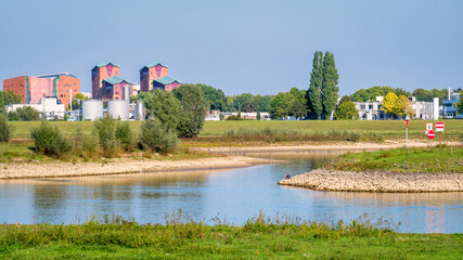 Dutch landscape with the river IJssel and its floodplains near the Hanze city of Deventer. Apartment buildings and industrial buildings can be seen. It is a warm and clear summer September day.