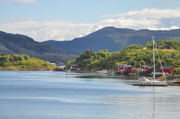 View from ferry to the small fishermen village with traditional red houses in Helgeland archipelago in the Norwegian sea
