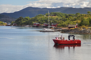 
View from ferry to the small fishermen village with traditional red houses in Helgeland archipelago in the Norwegian sea. Red boat in the foreground