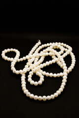 Long white pearl beads lie on a black background