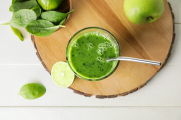 Glass of tasty green smoothie and ingredients on light wooden background