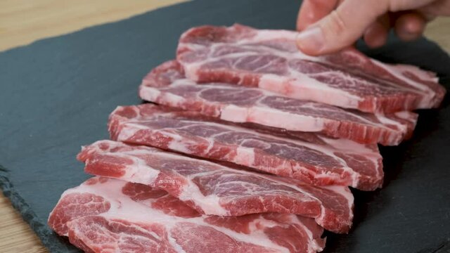 Young woman at the kitchen table lays red raw meat of beaf or pork. Female hands putting filet on stone board. Housewife is cooking at home interior. Concept of homemade food.