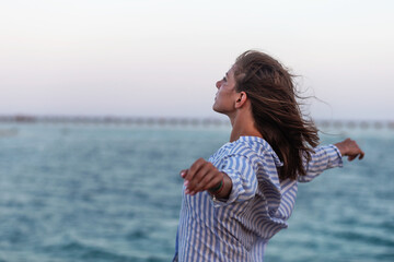 Woman enjoying freedom. Standing arms outstretched back and enjoy life on the beach at sea under sunlight sky.