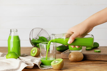 Woman pouring green smoothie from bottle into glass on table