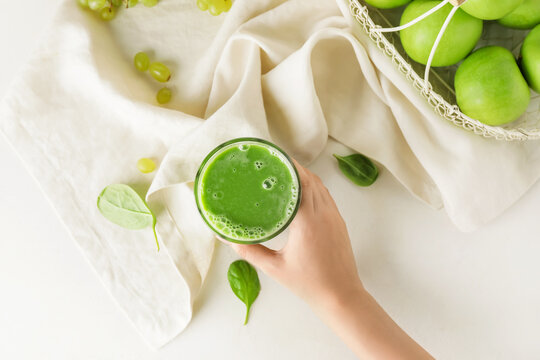 Woman holding glass of healthy green smoothie on light background