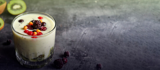 Yogurt with berry and kiwi in a glass. Fruit and berry smoothie. Milkshake with kiwi, raspberry, blueberry and banana Healthy food. Dark background. Copy space.