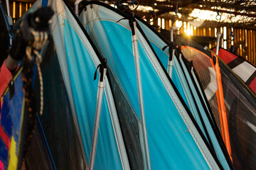 Windsurfing sails storage on a beach watersports facility. Surfer boards on shelf lie  under the roof for rental. Colorful sails background in sunlight