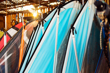 Windsurfing sails storage on a beach watersports facility. Surfer boards on shelf lie  under the roof for rental. Colorful sails background in sunlight