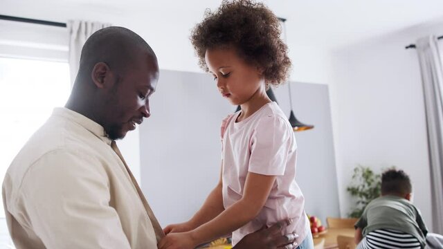 Small daughter helping father to get dressed at home, multi ethnic family.