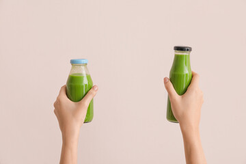 Woman holding bottles of healthy green smoothie on light background
