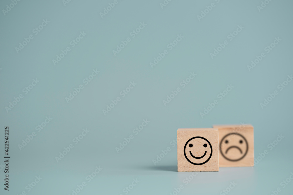 Poster Smiley face in front of sadness face which print screen on wooden cube block, emotion selection for customer satisfaction and evaluation concept.