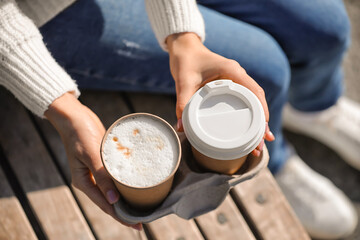 Woman with takeaway cups of tasty latte outdoors, closeup