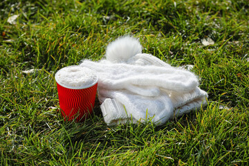 Takeaway cup of tasty latte, mittens and hat on grass