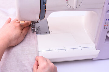 view of sewing process. Female hands stitching light fabric on sewing machine at home. Seamstress hands holding textile for bed linen. close-up