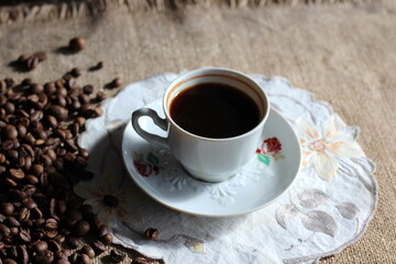 a cup of coffee and coffee beans are scattered on a linen napkin