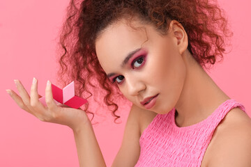 Beautiful young African-American woman with makeup sponges on color background