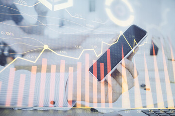 Double exposure of man's hands holding and using a digital device and forex graph drawing. Financial market concept.