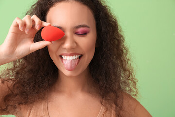 Beautiful young African-American woman with makeup sponge on color background