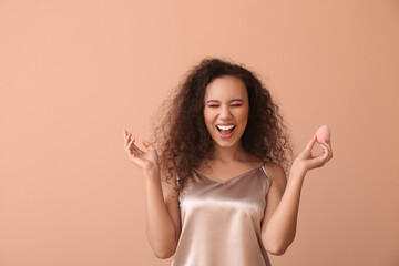 Beautiful young African-American woman with makeup sponge on color background