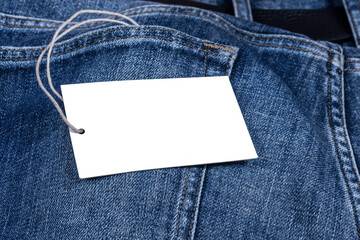 Empty clothes tag with white space for mockup lying on jeans background.