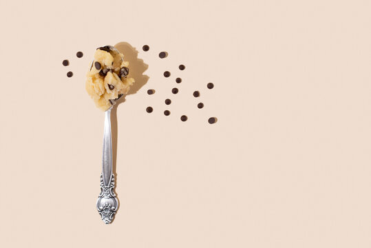 Edible cookie dough in spoon with chocolate chips on the yellow background in sunlight.